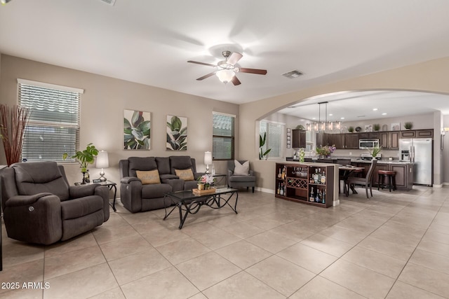 living area featuring light tile patterned floors, ceiling fan with notable chandelier, baseboards, arched walkways, and visible vents