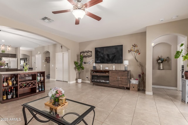 living area featuring visible vents, arched walkways, light tile patterned floors, and a ceiling fan