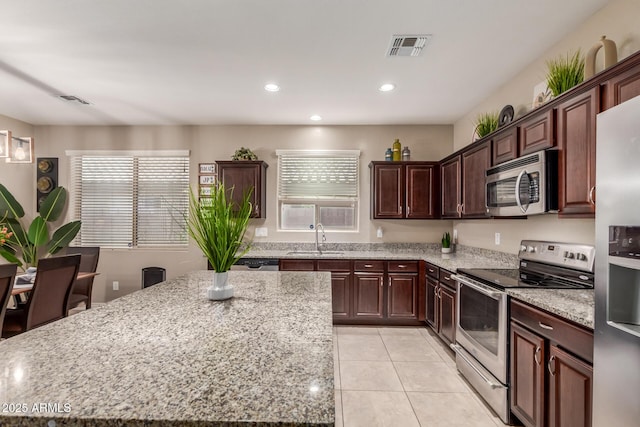kitchen with visible vents, stainless steel appliances, a kitchen island, a sink, and light tile patterned floors