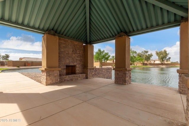 view of patio with a water view and an outdoor stone fireplace