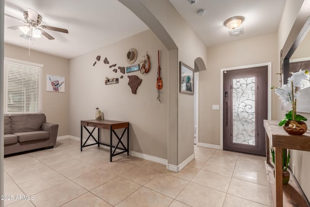 entryway with baseboards, arched walkways, light tile patterned floors, and a ceiling fan