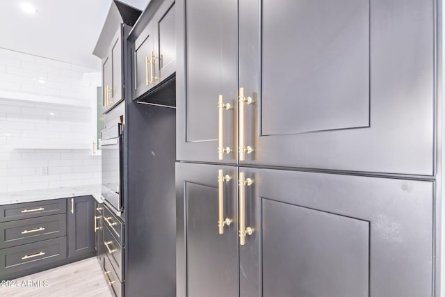 kitchen featuring light hardwood / wood-style flooring, gray cabinetry, light stone counters, decorative backsplash, and stainless steel oven