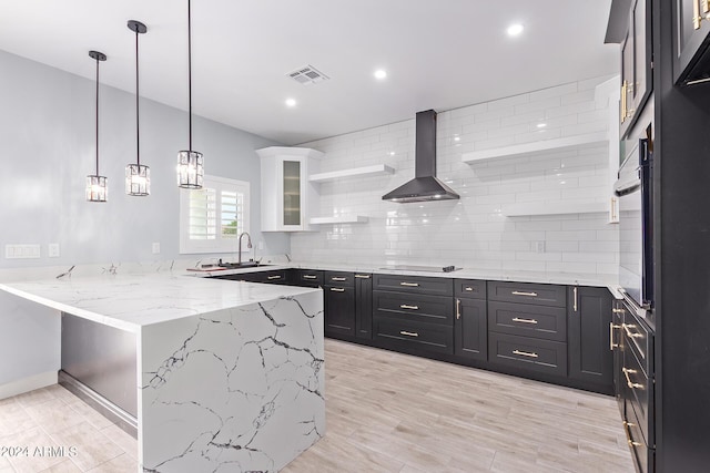 kitchen featuring wall chimney exhaust hood, sink, kitchen peninsula, light stone countertops, and white cabinets