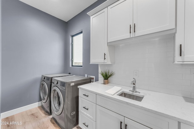 clothes washing area featuring sink, washing machine and dryer, light hardwood / wood-style floors, and cabinets