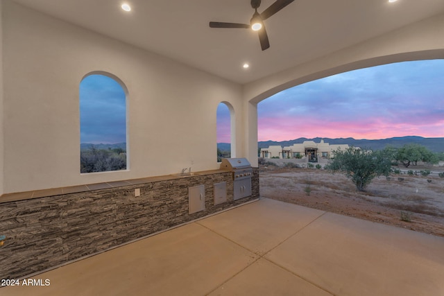 patio terrace at dusk featuring a mountain view, ceiling fan, an outdoor kitchen, and grilling area