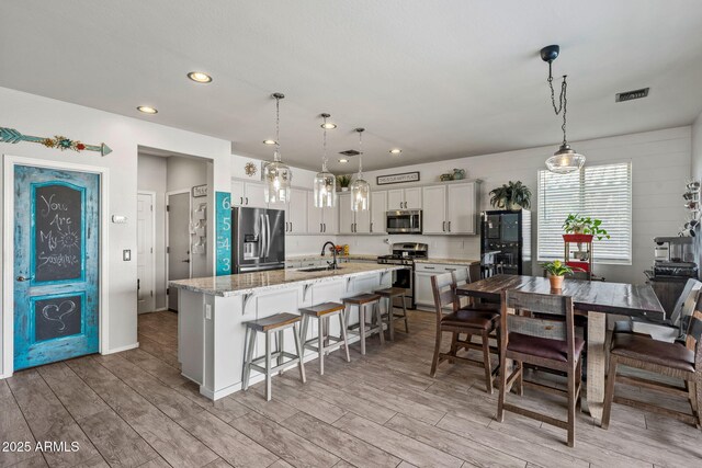 kitchen with hanging light fixtures, appliances with stainless steel finishes, sink, and a center island with sink