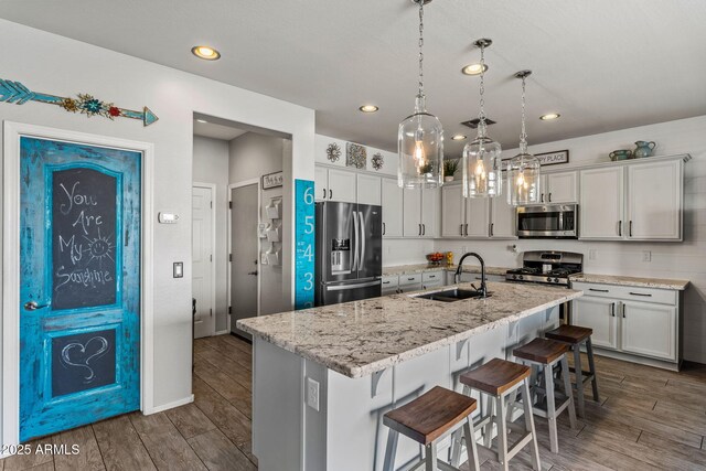 kitchen with decorative light fixtures, sink, light stone counters, stainless steel appliances, and a center island with sink