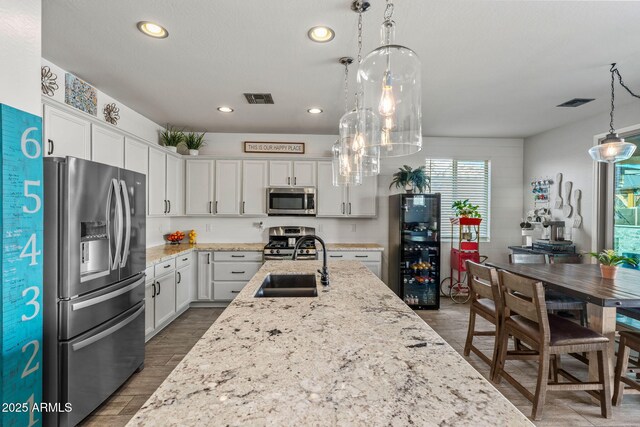 kitchen featuring decorative light fixtures, sink, white cabinets, stainless steel appliances, and light stone countertops