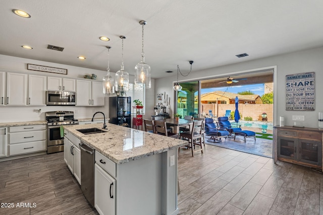 kitchen featuring appliances with stainless steel finishes, white cabinetry, sink, hanging light fixtures, and a kitchen island with sink