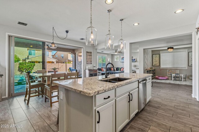 kitchen featuring white cabinetry, an island with sink, sink, hanging light fixtures, and light stone counters