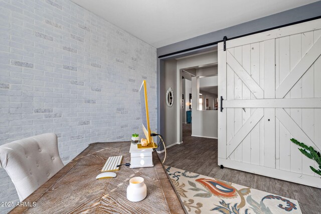 dining room featuring dark wood-type flooring, brick wall, and a barn door