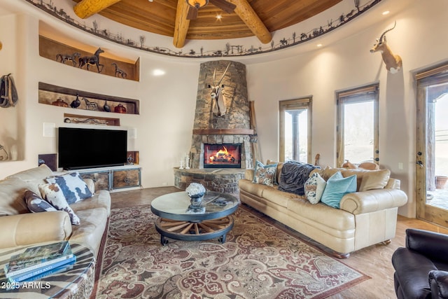 living room featuring beam ceiling, wooden ceiling, ceiling fan, a fireplace, and a high ceiling