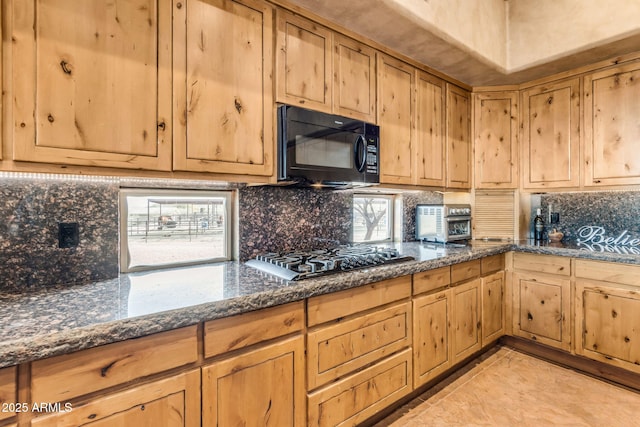 kitchen with tasteful backsplash, a healthy amount of sunlight, stainless steel gas stovetop, and dark stone countertops