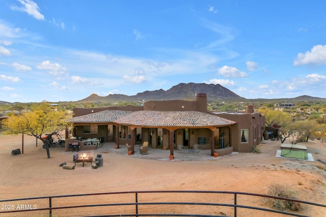 rear view of property with a mountain view, a patio area, and an outdoor fire pit