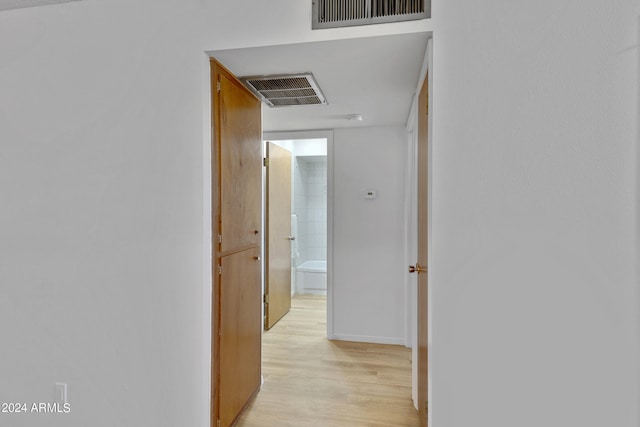 corridor with light wood-style flooring, visible vents, and baseboards