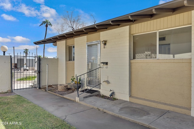 entrance to property with concrete block siding, a gate, and fence