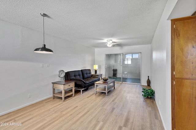 living room with ceiling fan, light wood finished floors, a textured ceiling, and baseboards