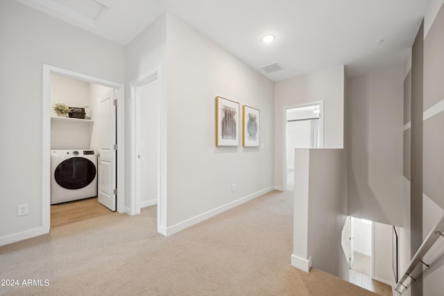 corridor with baseboards, visible vents, light carpet, and washer / dryer