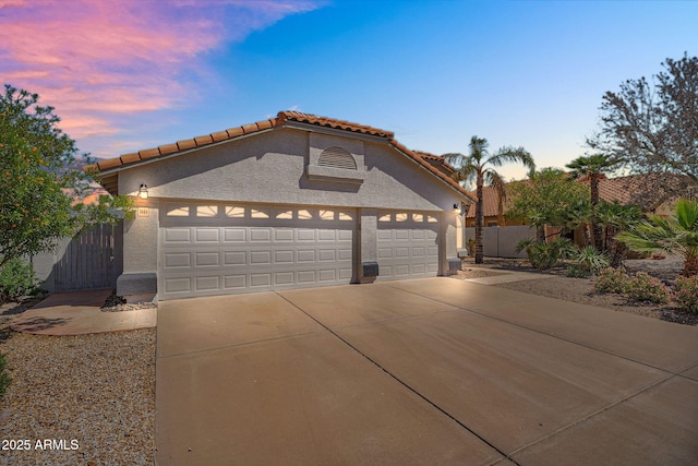 mediterranean / spanish home featuring stucco siding, a tiled roof, fence, and concrete driveway