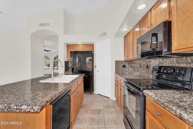 kitchen featuring black appliances, a sink, decorative backsplash, arched walkways, and dark stone countertops