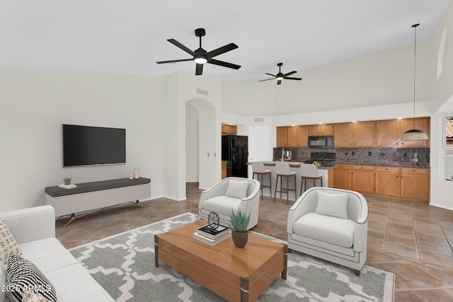 living area featuring arched walkways, a ceiling fan, baseboards, light tile patterned floors, and high vaulted ceiling