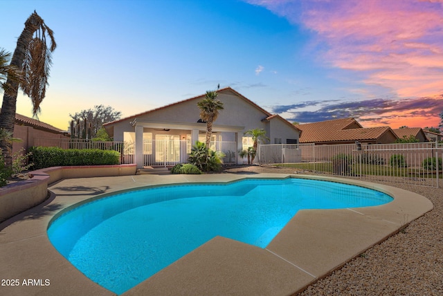 pool at dusk featuring fence and a patio