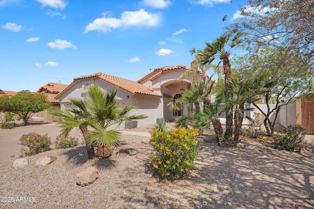 mediterranean / spanish home featuring a tiled roof, stucco siding, and fence