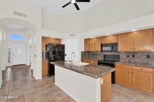 kitchen with black appliances, a towering ceiling, a sink, arched walkways, and backsplash