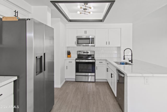 kitchen featuring stainless steel appliances, a tray ceiling, sink, light hardwood / wood-style flooring, and white cabinetry