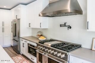 10266 E Caron St, Scottsdale, AZ 85258 - kitchen with appliances with stainless steel finishes, wall chimney exhaust hood, white cabinets, recessed lighting, and light wood-style flooring