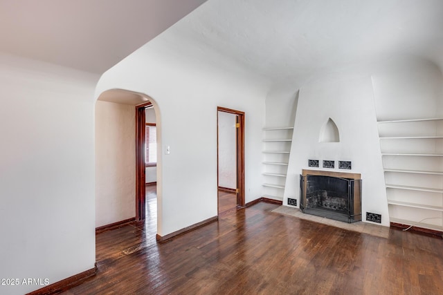 unfurnished living room featuring dark wood-type flooring and built in features