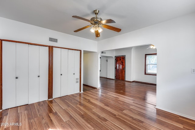 unfurnished bedroom featuring ceiling fan, dark wood-type flooring, and multiple closets