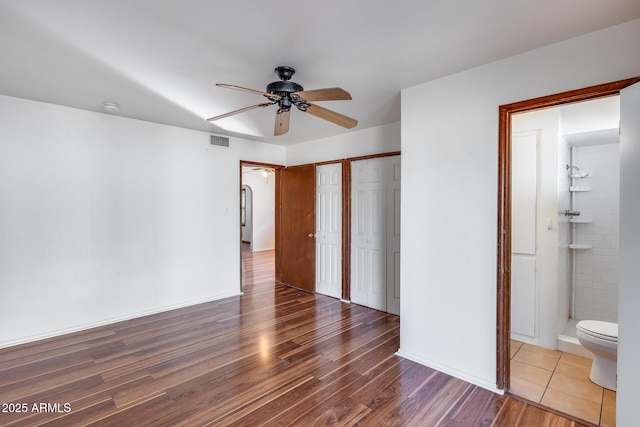 unfurnished bedroom featuring multiple closets, wood-type flooring, connected bathroom, and ceiling fan