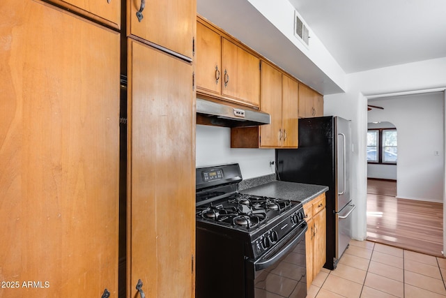 kitchen with black gas range oven, light tile patterned floors, and stainless steel refrigerator