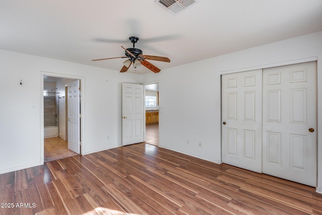 unfurnished bedroom with dark wood-type flooring, ceiling fan, connected bathroom, and a closet