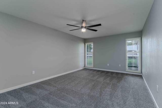 spare room featuring a ceiling fan, dark colored carpet, and baseboards