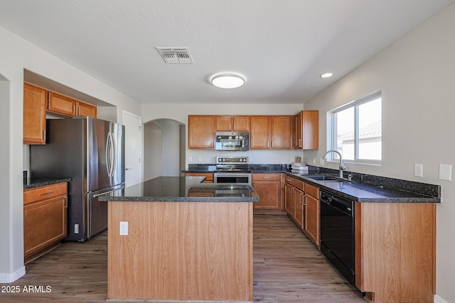 kitchen featuring stainless steel appliances, a sink, visible vents, a center island, and dark wood finished floors