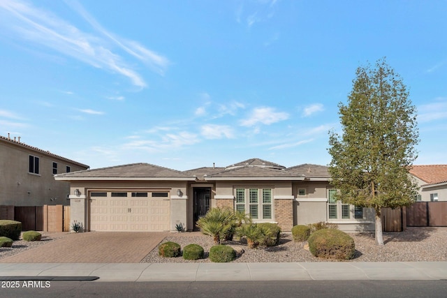 prairie-style house featuring an attached garage, fence, decorative driveway, and stucco siding