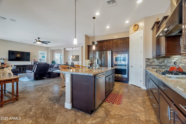 kitchen with a sink, visible vents, wall chimney range hood, appliances with stainless steel finishes, and backsplash