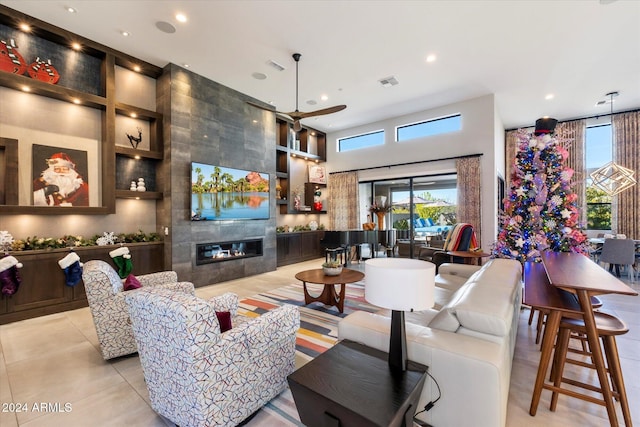 tiled living room featuring built in shelves, a tile fireplace, ceiling fan, and a high ceiling