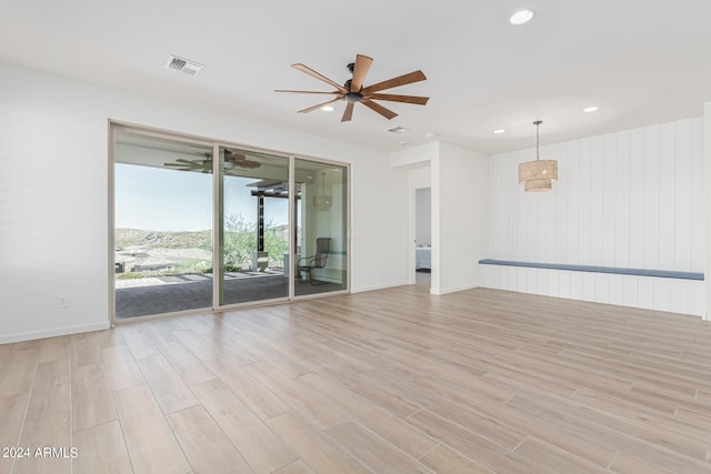 unfurnished room featuring ceiling fan, light wood-type flooring, and wood walls