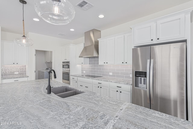 kitchen featuring wall chimney range hood, independent washer and dryer, hanging light fixtures, appliances with stainless steel finishes, and white cabinetry