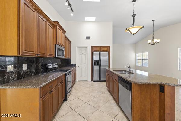 5450 E Paradise Ln, Scottsdale, AZ 85254 - kitchen with appliances with stainless steel finishes, brown cabinetry, tasteful backsplash, light tile patterned floors, and dark stone counters