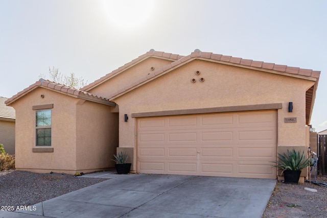 mediterranean / spanish house featuring driveway, an attached garage, a tile roof, and stucco siding