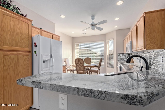 kitchen with white appliances, light stone counters, backsplash, and recessed lighting