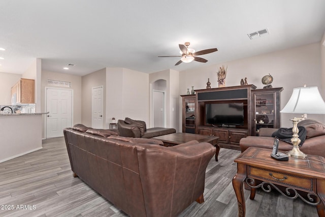 living room featuring baseboards, visible vents, arched walkways, a ceiling fan, and light wood-style flooring