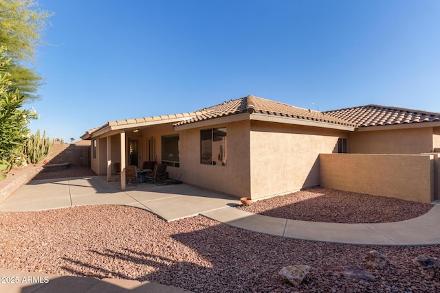 rear view of house featuring fence, a patio, a tiled roof, and stucco siding