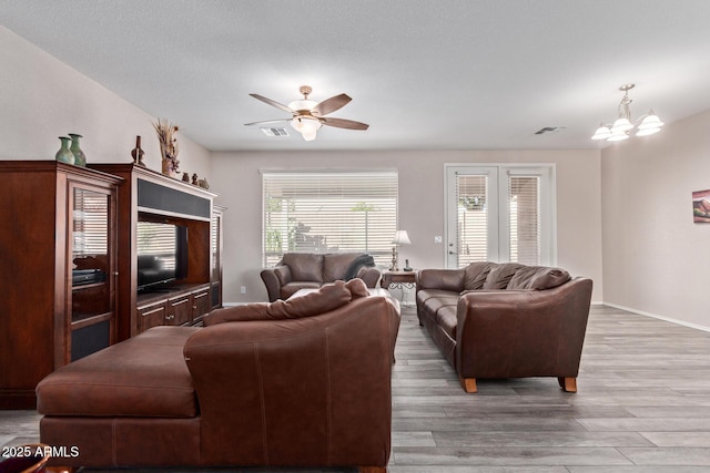 living room with visible vents, light wood-style flooring, baseboards, and ceiling fan with notable chandelier