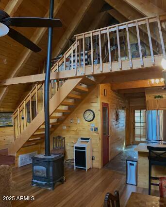 interior space with ceiling fan, wood walls, high vaulted ceiling, and wood finished floors