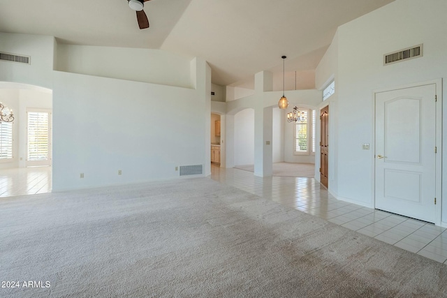 empty room with ceiling fan with notable chandelier, light tile patterned floors, and high vaulted ceiling